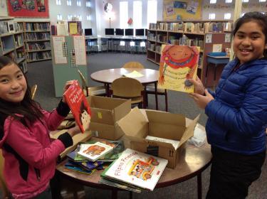 children in library holding up books 